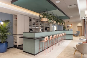 A modern bar area with a long counter, multiple stools, and shelves with glasses and bottles. - Hampton By Hilton Paris Saint Ouen (Saint-Ouen)