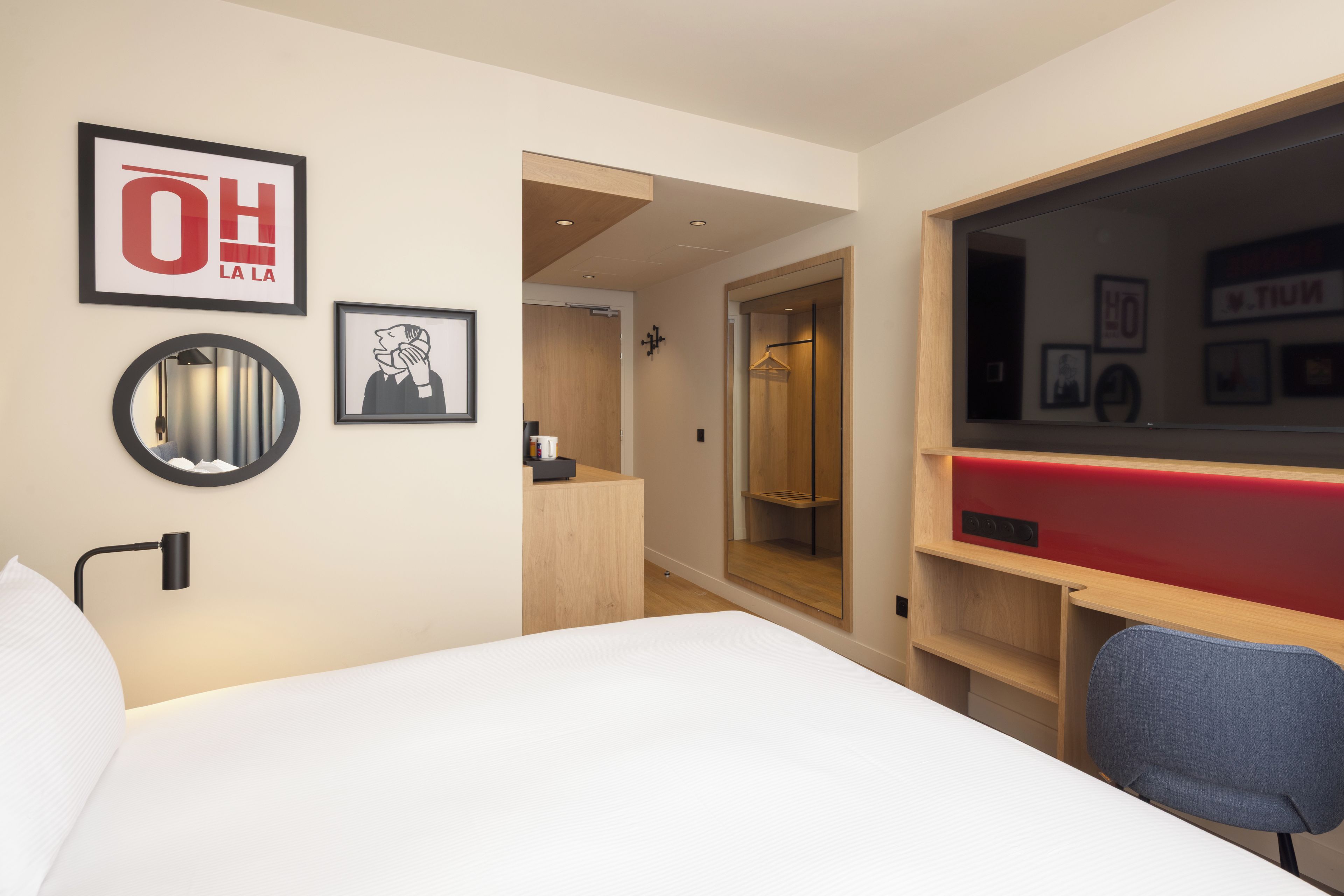 Una habitación de hotel con una cama, un escritorio, un espejo y un armario.