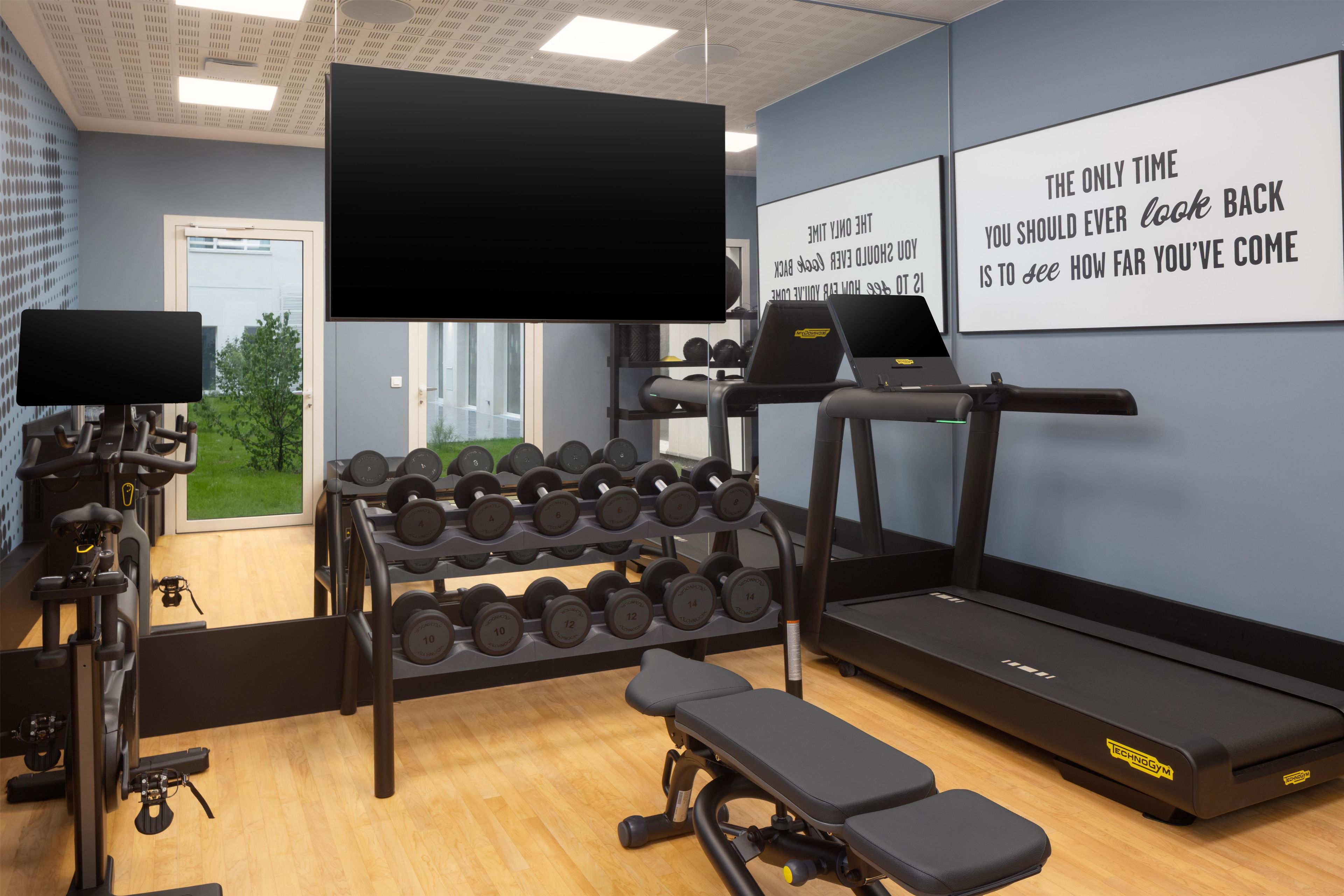 Un gimnasio con equipo de ejercicio, cinta de correr, mancuernas y carteles de motivación en la pared.