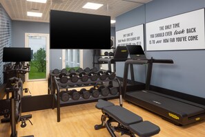 Un gimnasio con equipo de ejercicio, cinta de correr, mancuernas y carteles de motivación en la pared.