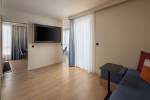 Uma sala de estar moderna com televisão de tela plana na parede, um sofá, uma mesinha e uma área de jantar com uma cadeira.