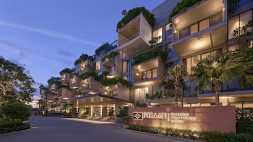 A multi-story hotel with balconies, a well-lit entrance, and a sign indicating it's part of the NHAAN TAPESTRY COLLECTION by Hilton.