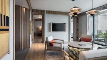 Una habitación de hotel moderna con una televisión, una mesa de centro redonda, un sofá y un balcón con mobiliario exterior.