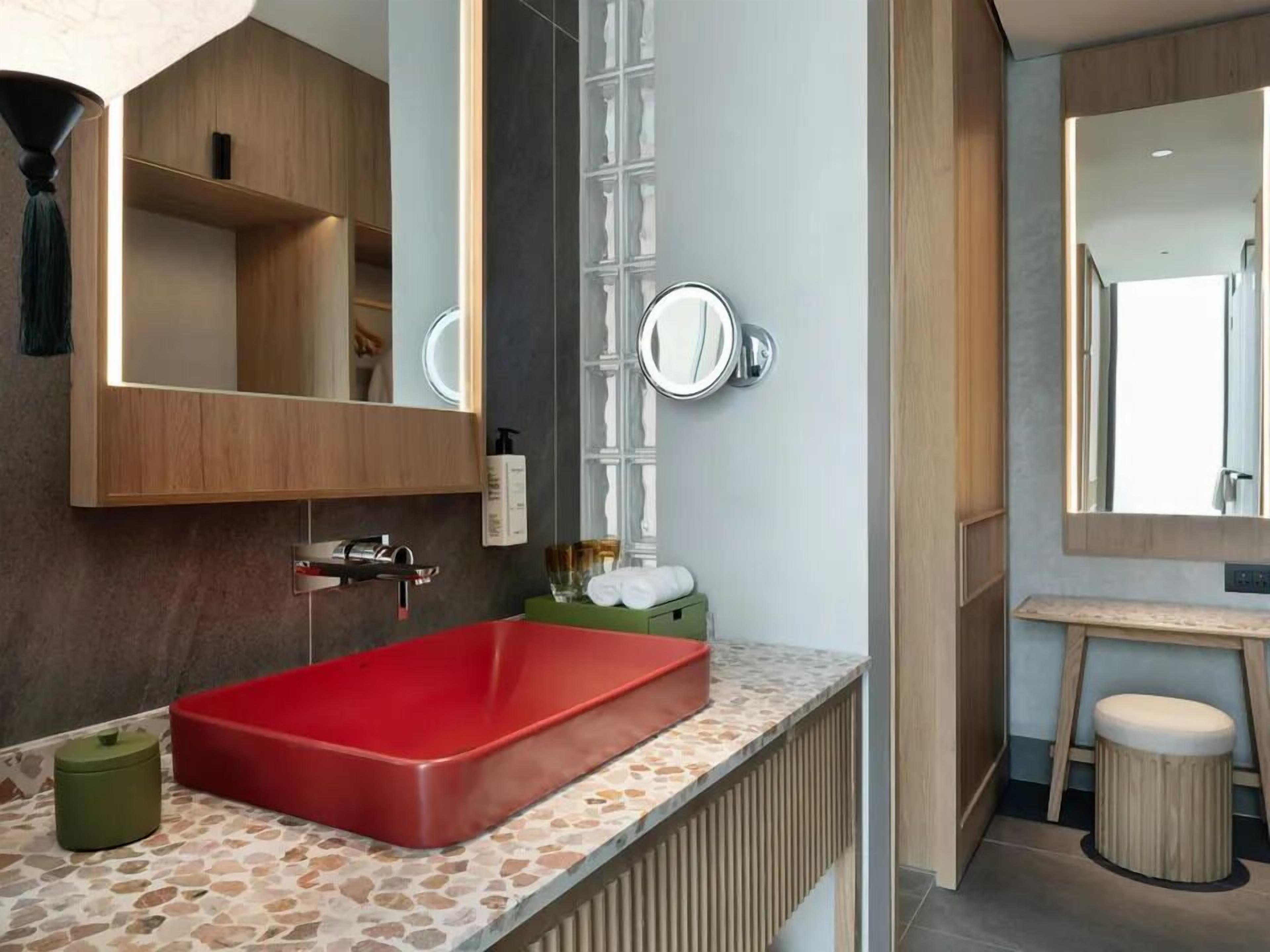 Ein Badezimmer mit einem roten Waschbecken, einem Spiegel und einer Holz-Waschkommode.