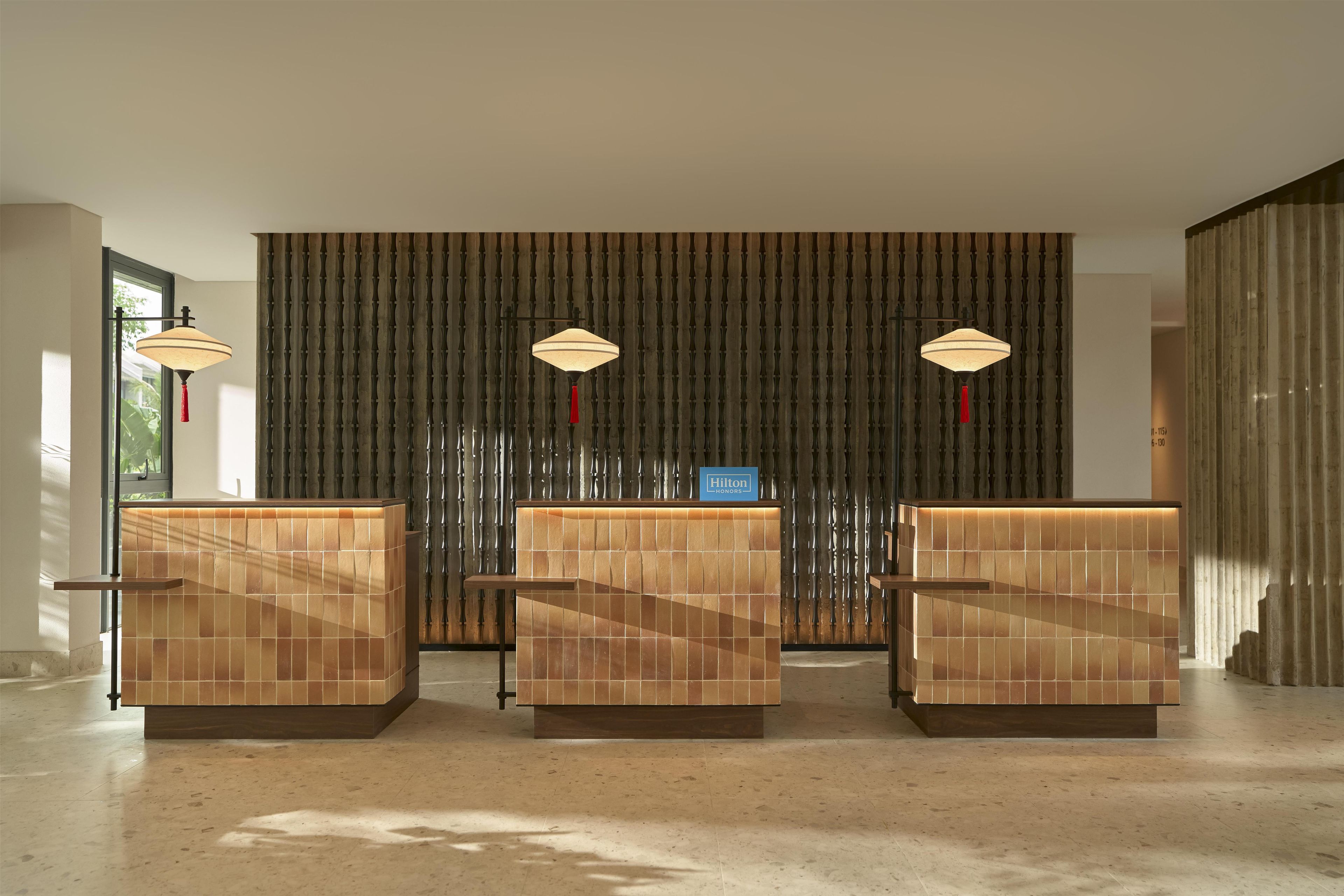 Zona de recepción con tres mostradores de madera, pared con motivo de bambú y dos lámparas colgantes.