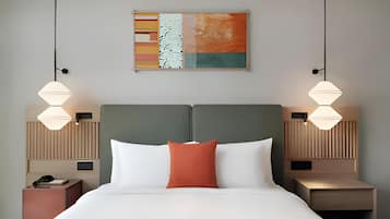 A hotel room with a large bed, two bedside tables, a wall-mounted painting, and pendant lights.