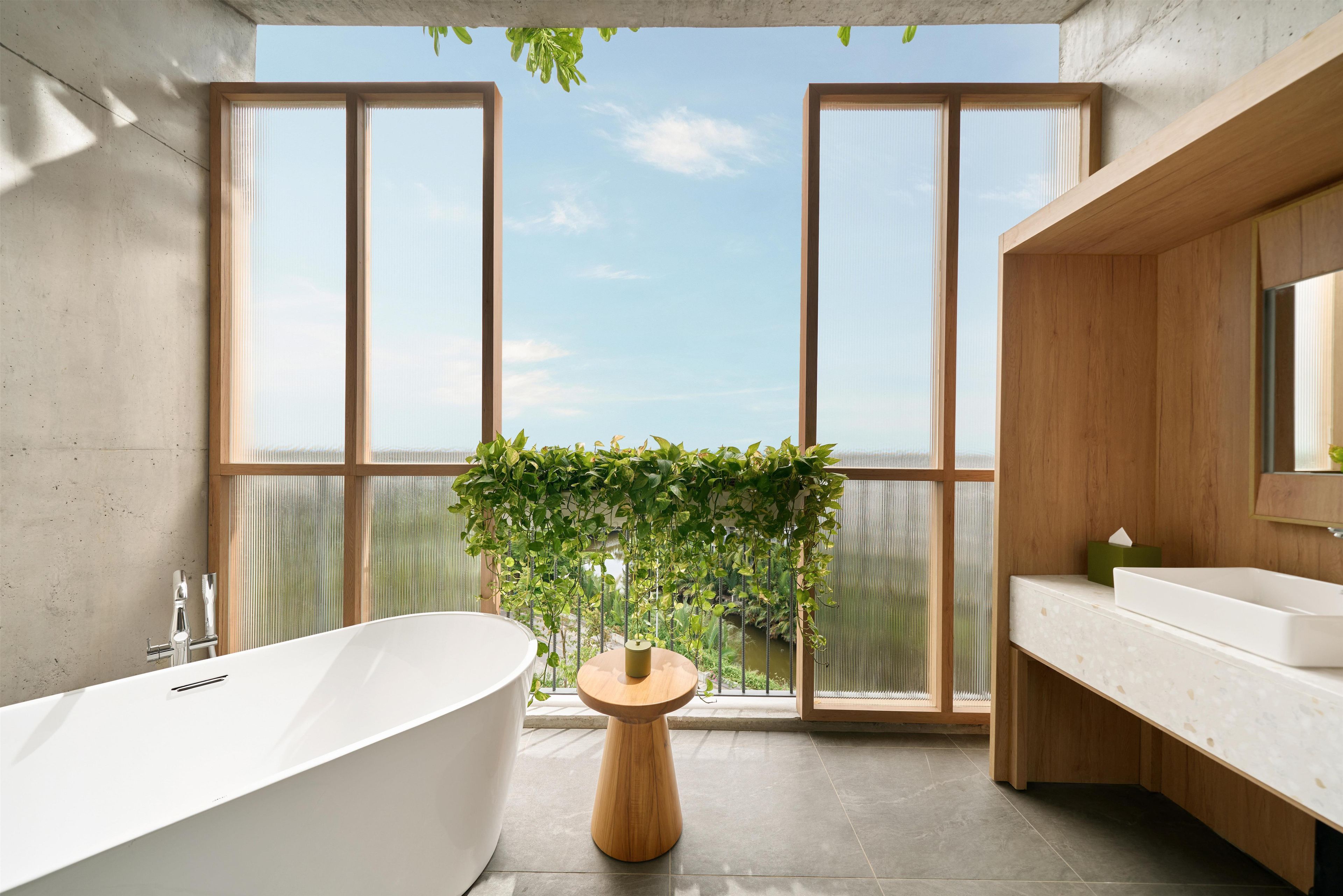 A modern bathroom with a freestanding bathtub, a wooden vanity, and a large window with a view of greenery.
