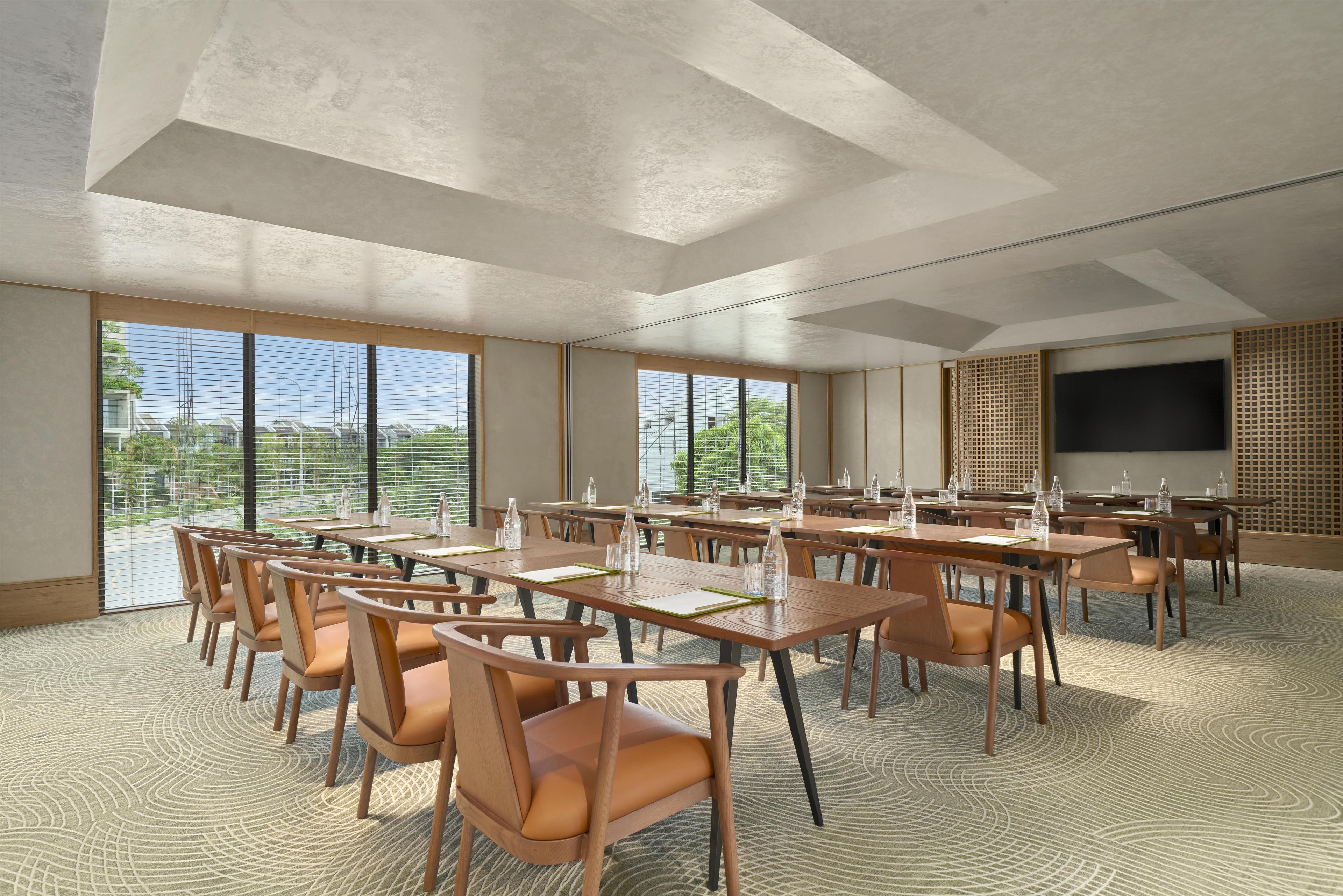 A spacious conference room with large tables and chairs, a flat-screen TV, and large windows offering a view of the outdoors.