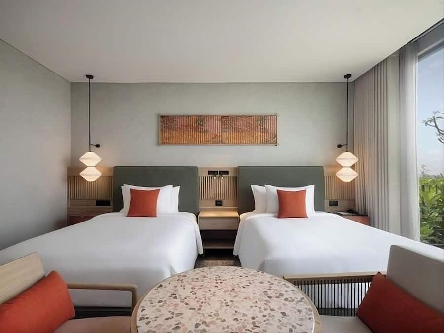 A hotel room with two beds, a round table, and a large window.