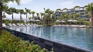 A swimming pool with lounge chairs and umbrellas, surrounded by palm trees and a multi-story building. - NHAAN Resort & Spa Hoi An, Tapestry Collection by Hilton (Hoi An)