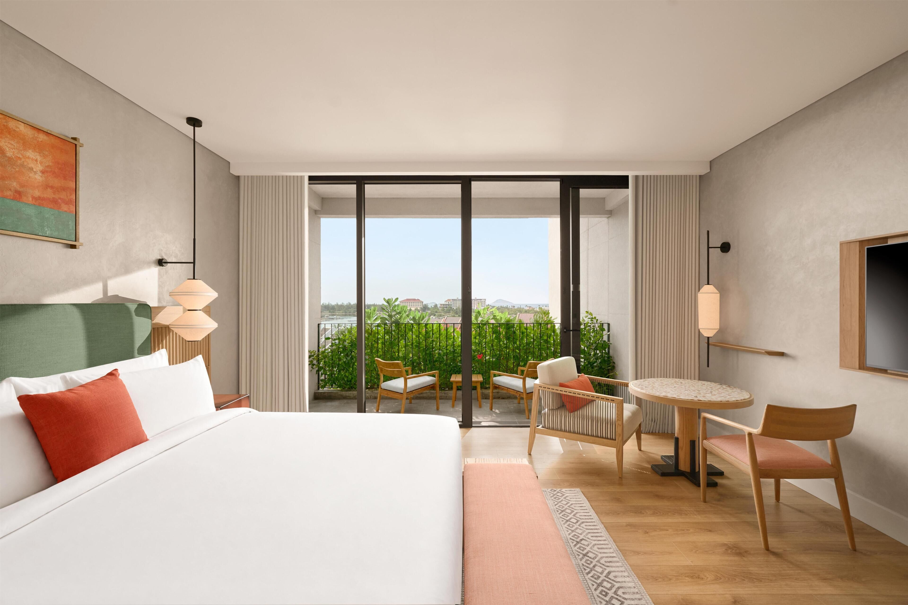 Habitación de hotel con una cama grande, un balcón con asientos y vista a la ciudad.