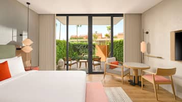 A hotel room with a large bed, a seating area with a table, and a view of a landscaped outdoor area.