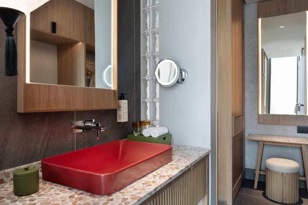 Un baño con un lavamanos rojo, armarios de madera, un espejo y un taburete pequeño.