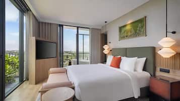A modern hotel room with a large bed, a TV, a sofa, a small table, and a balcony with a view.