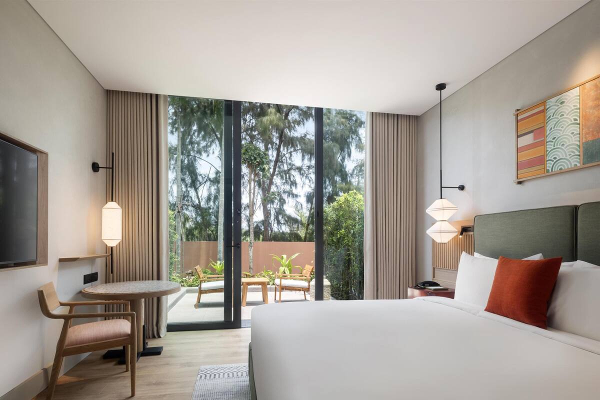 Habitación de hotel con una cama grande, un escritorio con silla, un televisor y vistas al exterior.