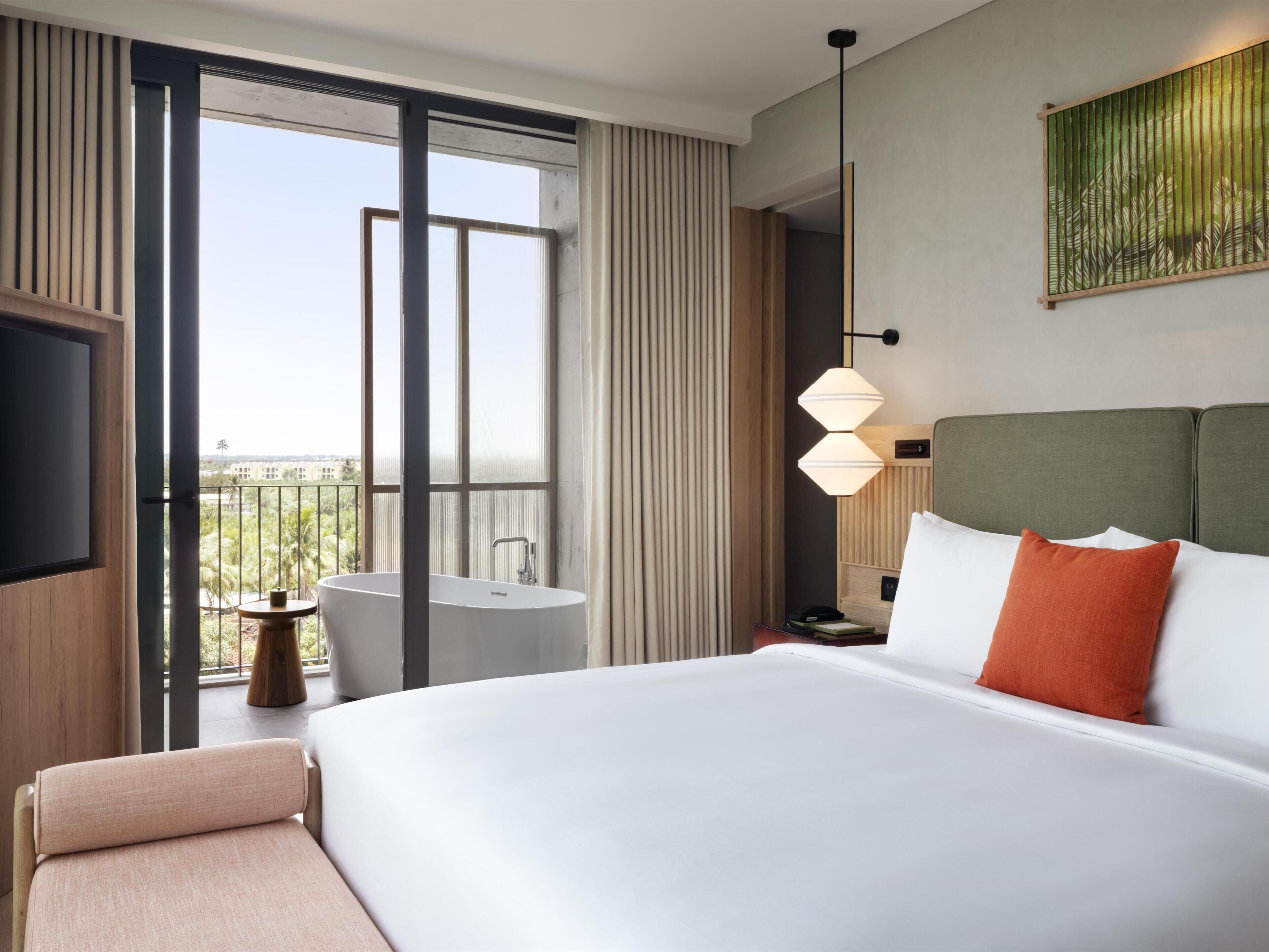 Ein Hotelzimmer mit einem großen Bett, einem kleinen runden Tisch, einer Badewanne und einem Balkon mit Blick.