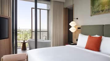 Ein Hotelzimmer mit einem großen Bett, einem kleinen runden Tisch, einer Badewanne und einem Balkon mit Blick.