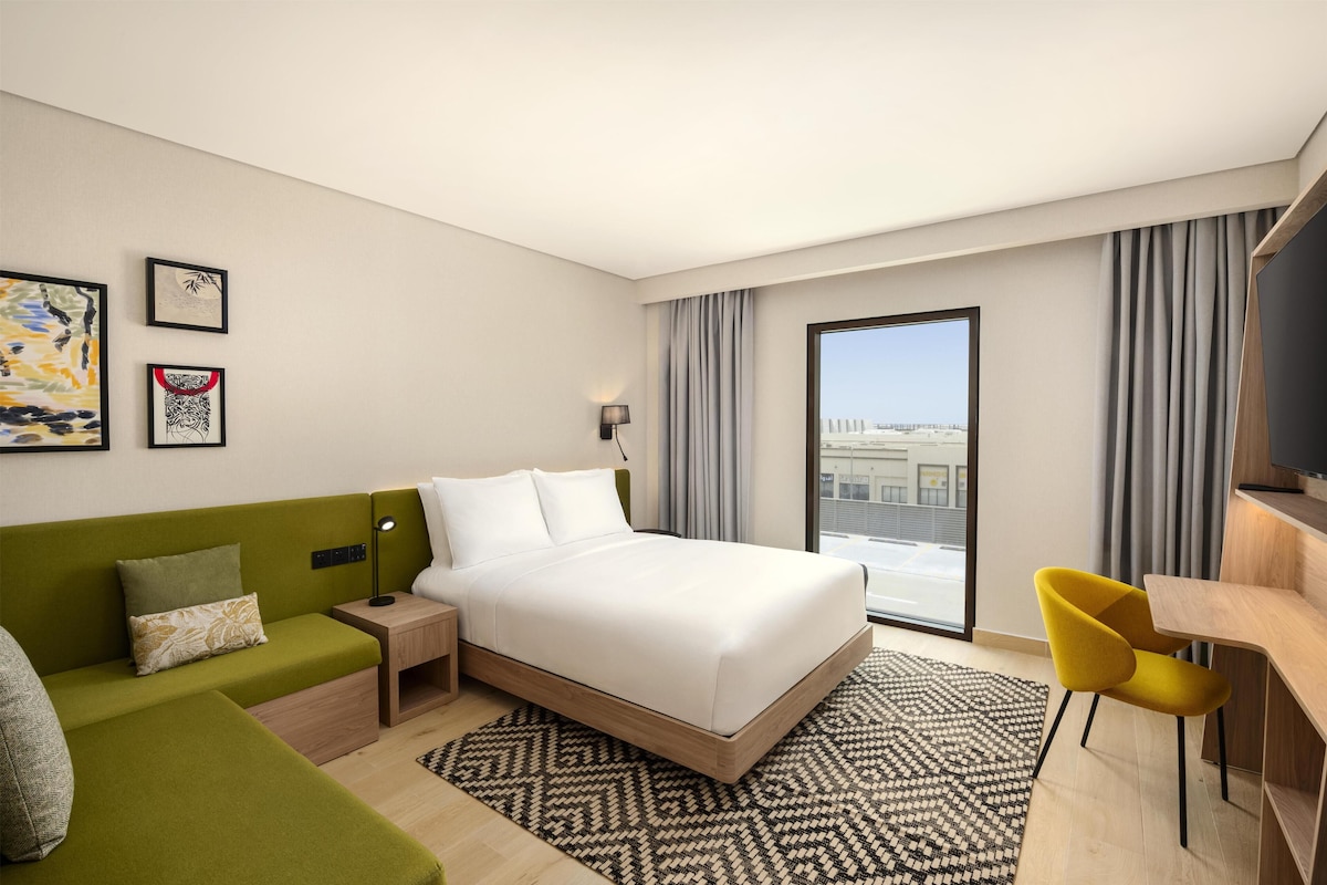 A modern hotel room with a bed, a green sofa, a desk, and a chair.