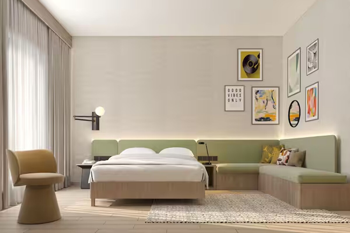 A modern hotel room with a bed, a seating area, a desk, and artwork on the walls.