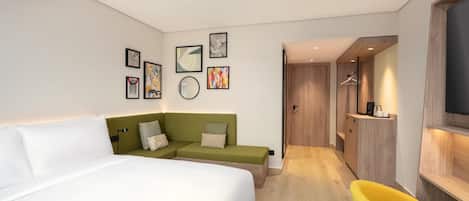 Ein modernes Hotelzimmer mit einem großen Bett, einem grünen Sofa, einem gelben Sessel und einem begehbaren Kleiderschrank.