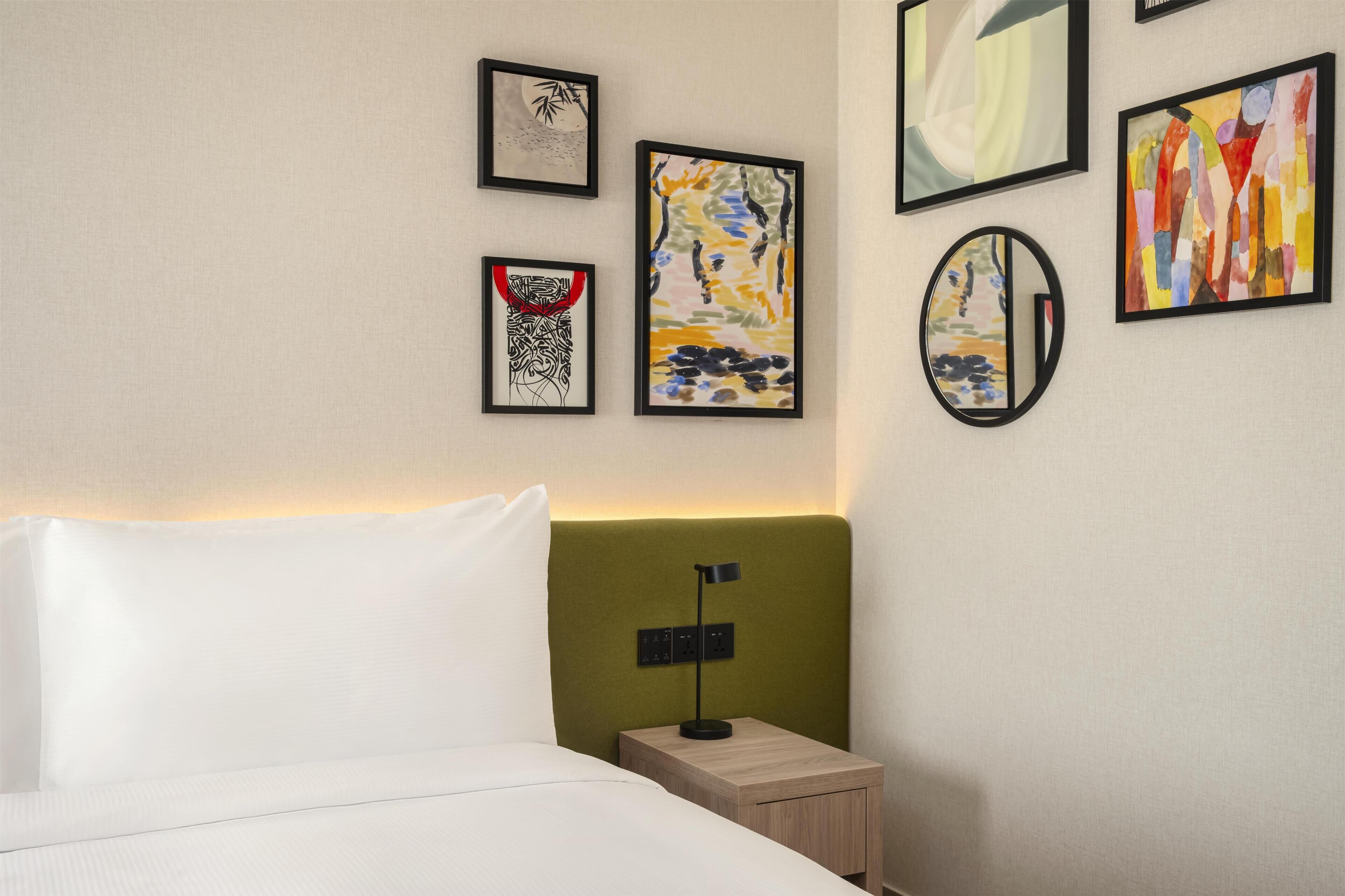 A hotel room with a bed, a nightstand, a lamp, and four framed artworks on the wall.
