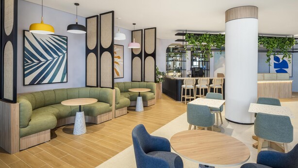 A modern lounge area with a green sofa, round tables, and a reception desk. - Hampton By Hilton Jeddah Souq7 (Jeddah)