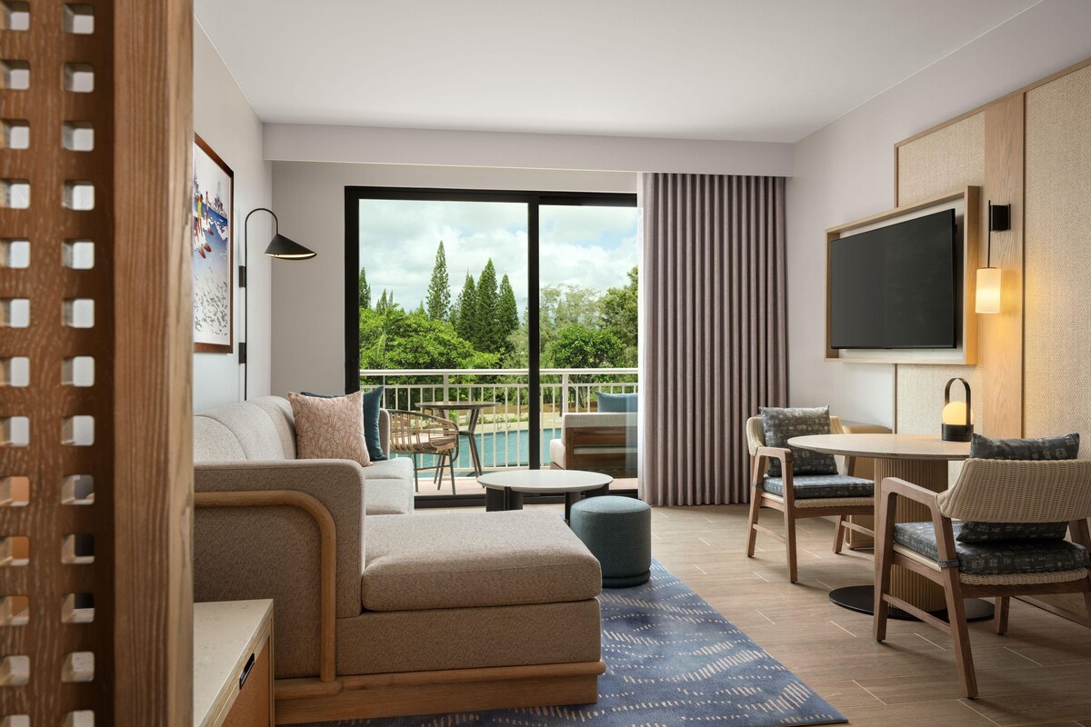 Een moderne woonkamer met een bank, stoelen, een salontafel, een televisie en een balkon met uitzicht op een zwembad.
