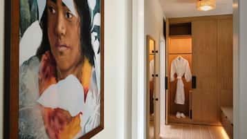 A hallway with a framed artwork on the wall, a wooden door with a robe and slippers hanging on it, and a ceiling light fixture.