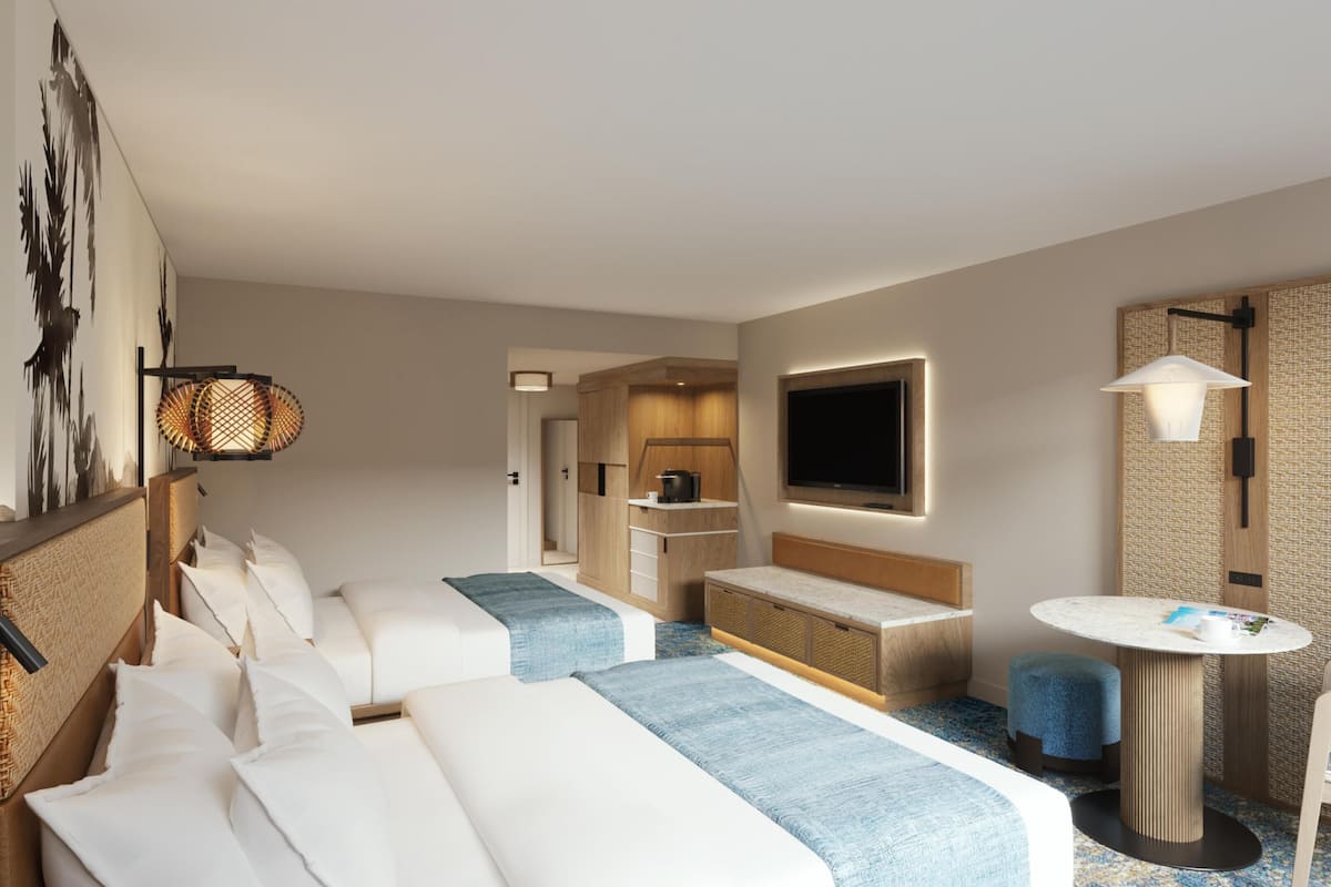 Habitación de hotel con dos camas, una kitchenette pequeña, televisión y una mesa redonda.