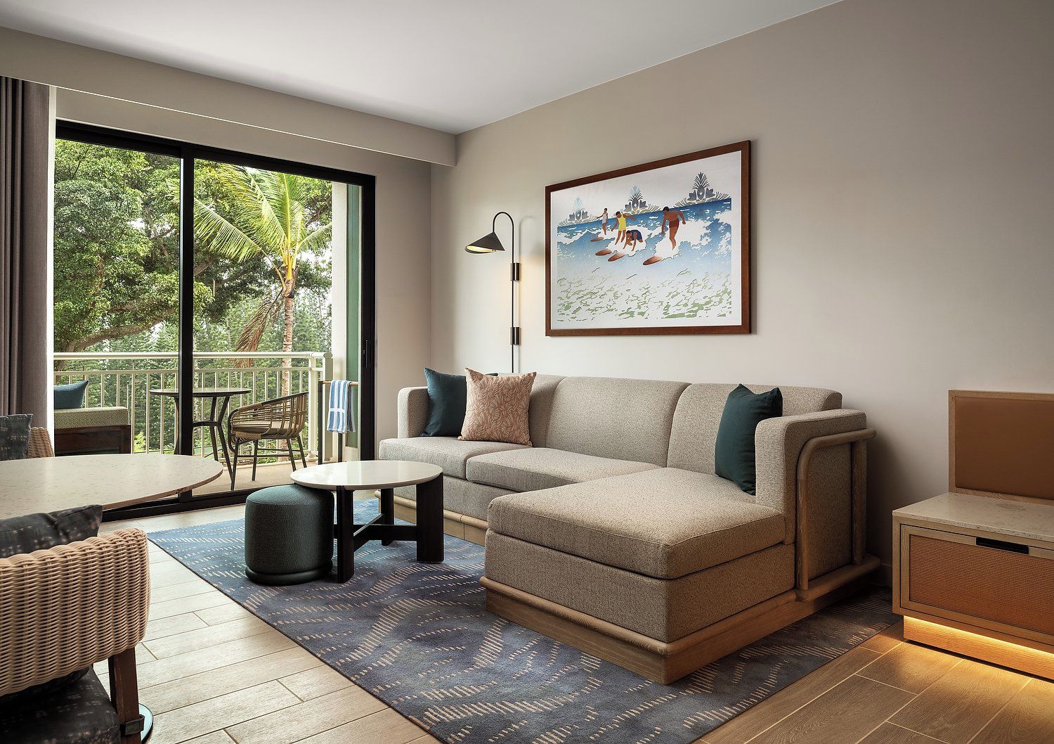 A modern living room with a sofa, a coffee table, and a dining area. There is a large window providing a view of the outdoors.