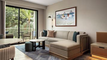 A modern living room with a sofa, a coffee table, and a dining area. There is a large window providing a view of the outdoors.