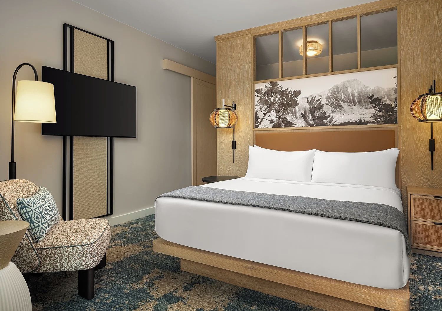 A hotel room with a large bed, a television, a seating area with a chair, and a wall-mounted artwork.