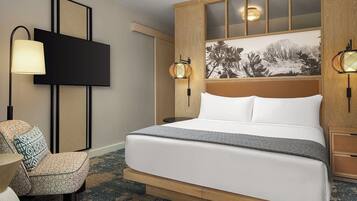A hotel room with a large bed, a television, a seating area with a chair, and a wall-mounted artwork.