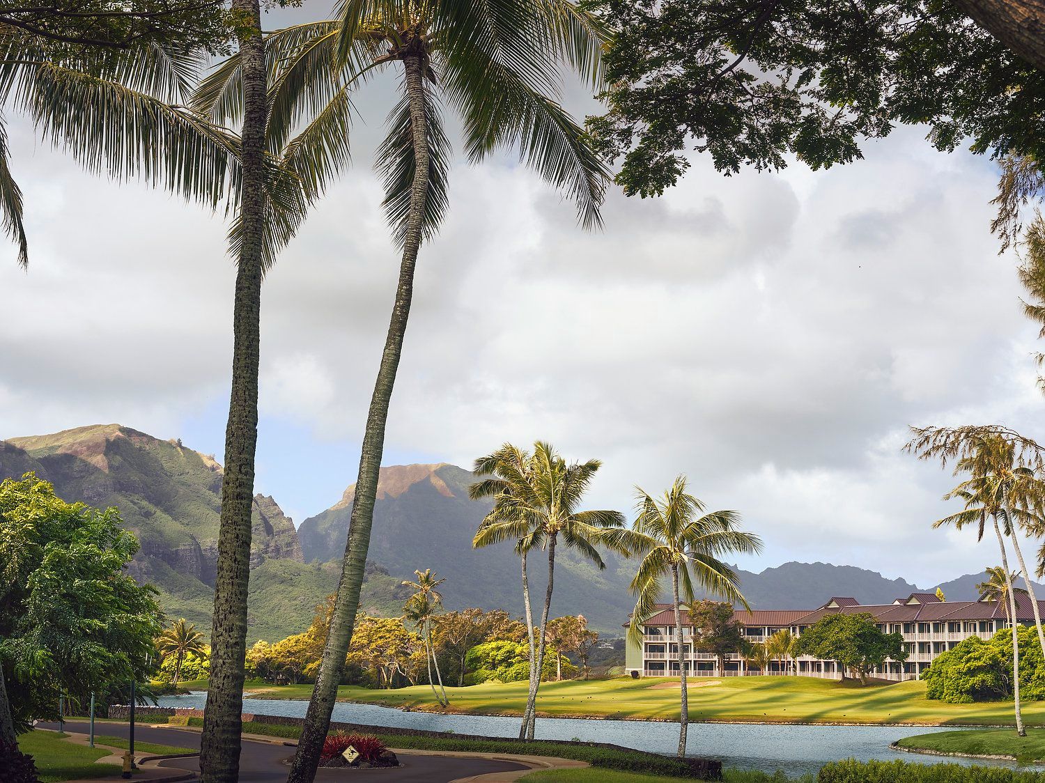 A golf course with palm trees, a body of water, and mountains in the background.