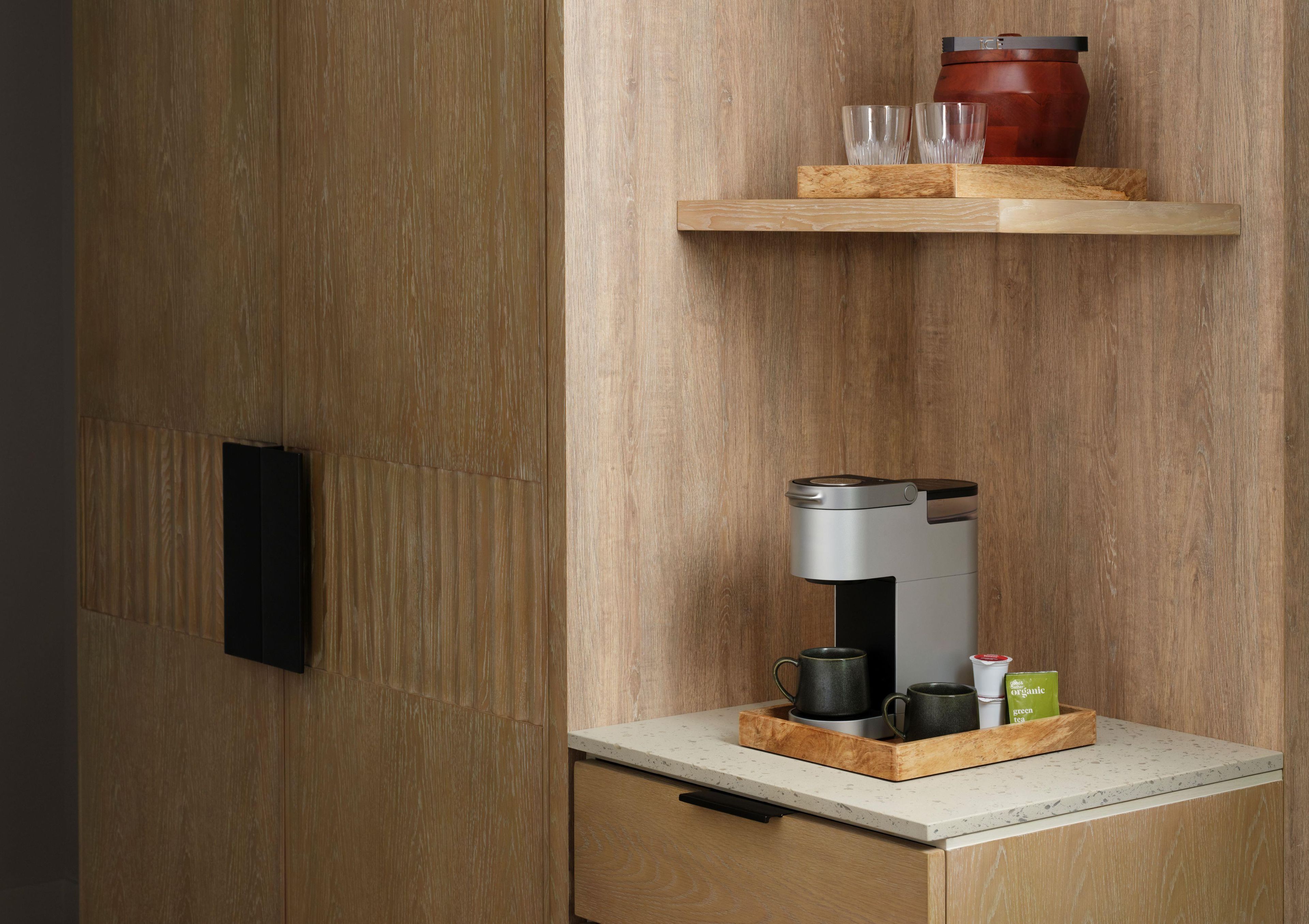 A kitchen area with a coffee machine, a red pot, and a tray with cups and a green tea box.