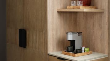 A kitchen area with a coffee machine, a red pot, and a tray with cups and a green tea box.