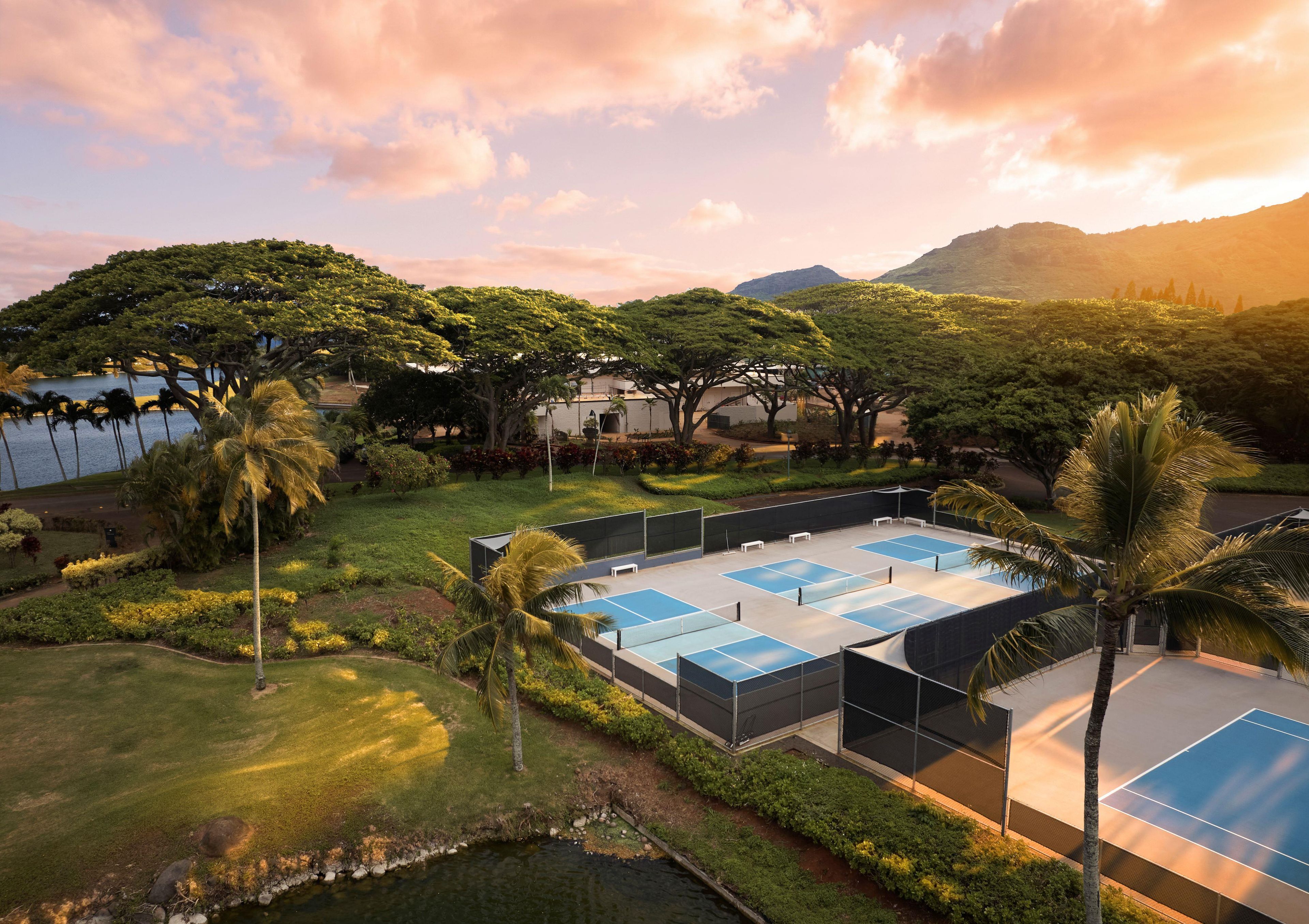 A tennis court surrounded by lush greenery and a body of water.