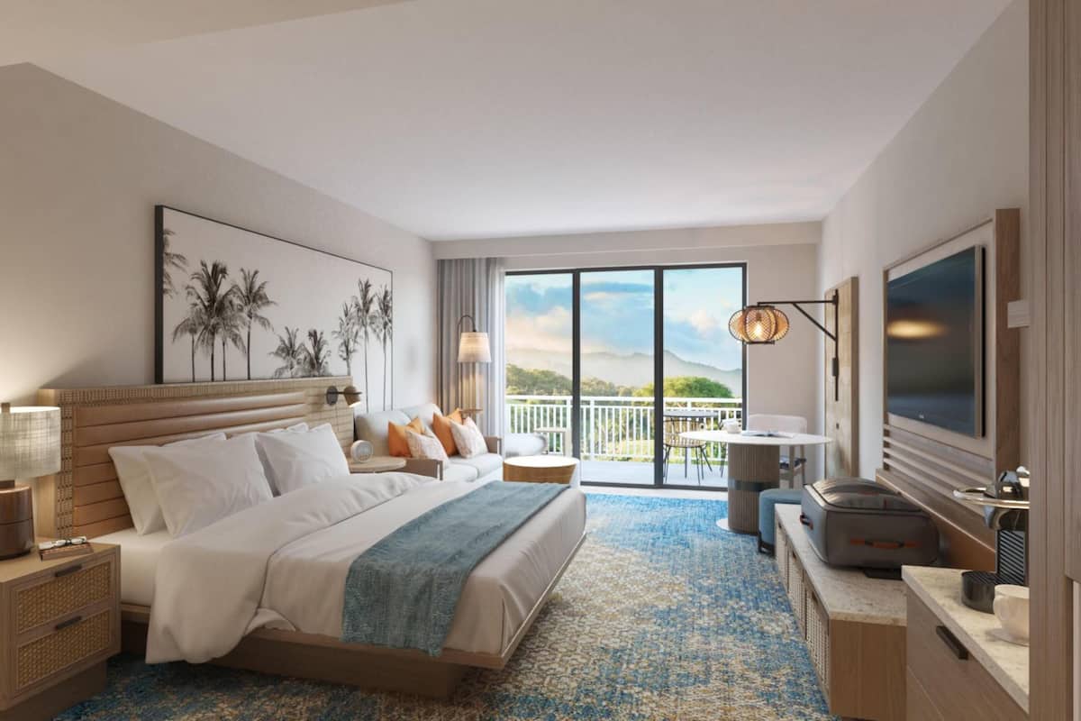 Habitación de hotel con cama, televisión, balcón con vistas y escritorio con lámpara.