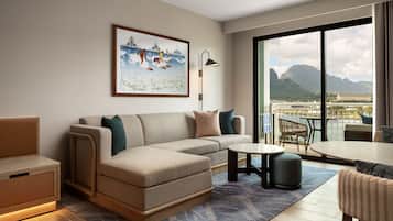 Quarto de hotel moderno com sofá, uma mesinha e vista para a água e montanhas.