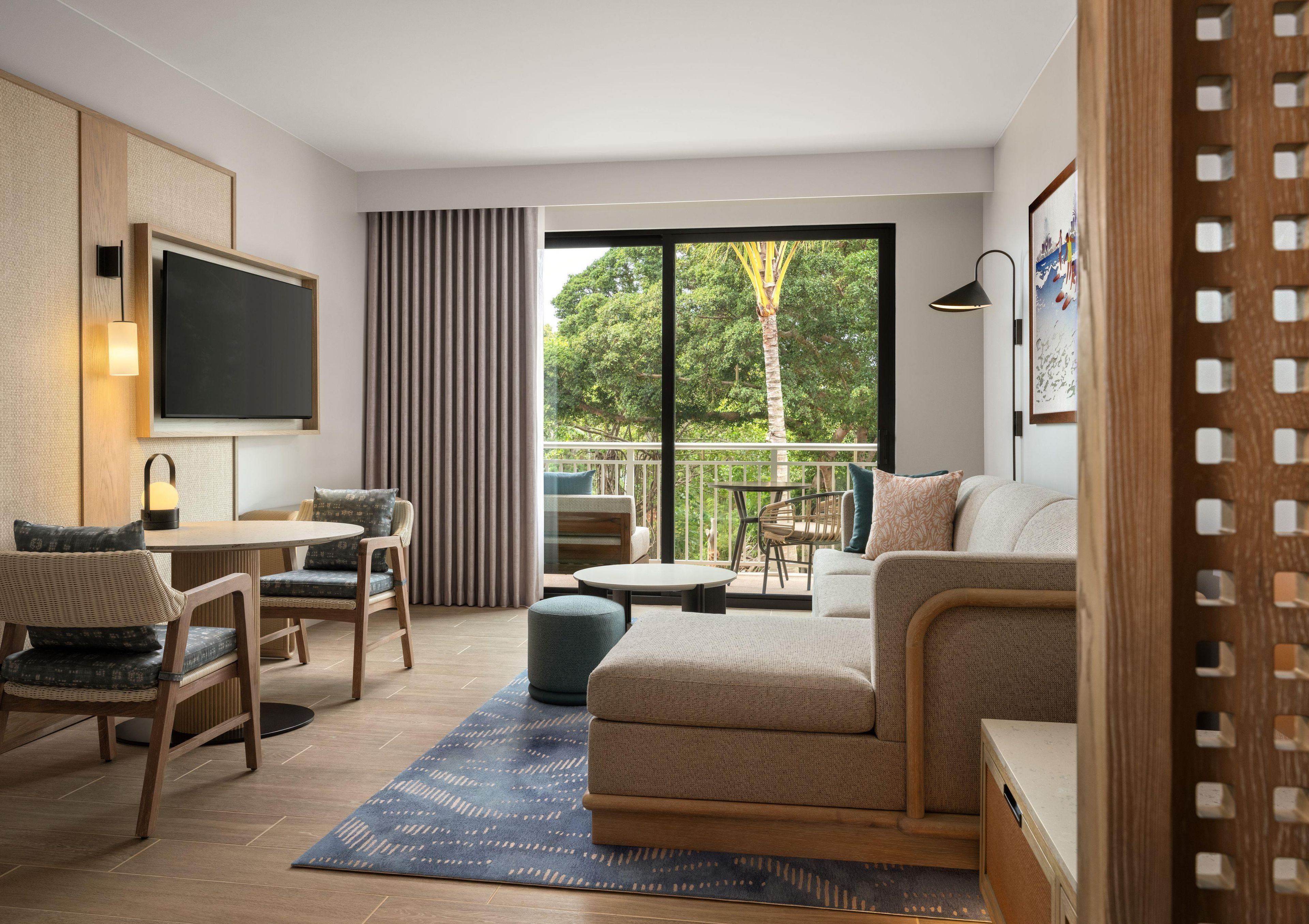 Una sala de estar moderna con sofá, sillones, televisor y un balcón con vista a árboles.
