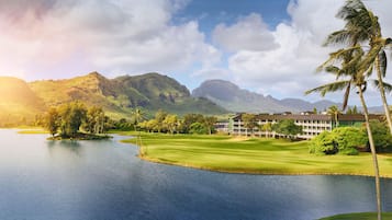 A golf course with a water body, palm trees, and a mountain backdrop.