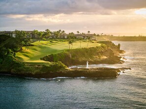 A coastal golf course with a lighthouse, ocean views, and a building complex in the background.