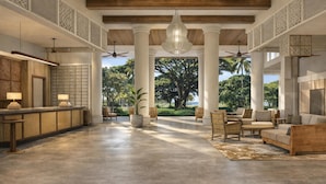 A spacious lobby with a reception desk, seating area, and large windows offering a view of greenery. - Hale Hokuala Kauai, Curio Collection By Hilton (Lihue)