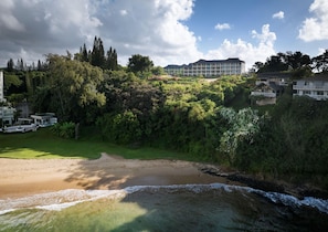 Ett hotell vid kusten med utsikt över stranden, frodig grönska och en klar himmel.