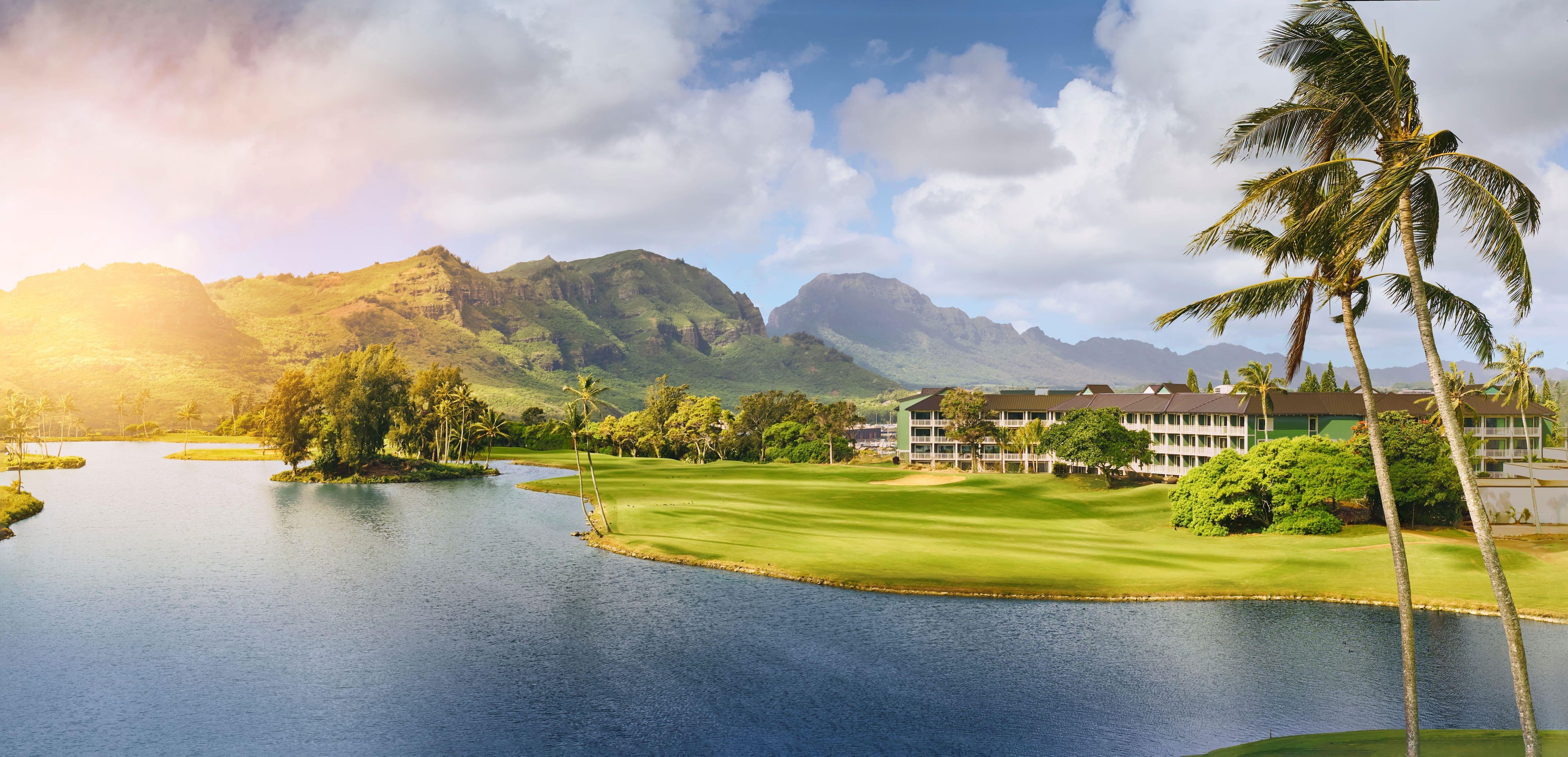 A golf course with a water body, palm trees, and a mountain backdrop.