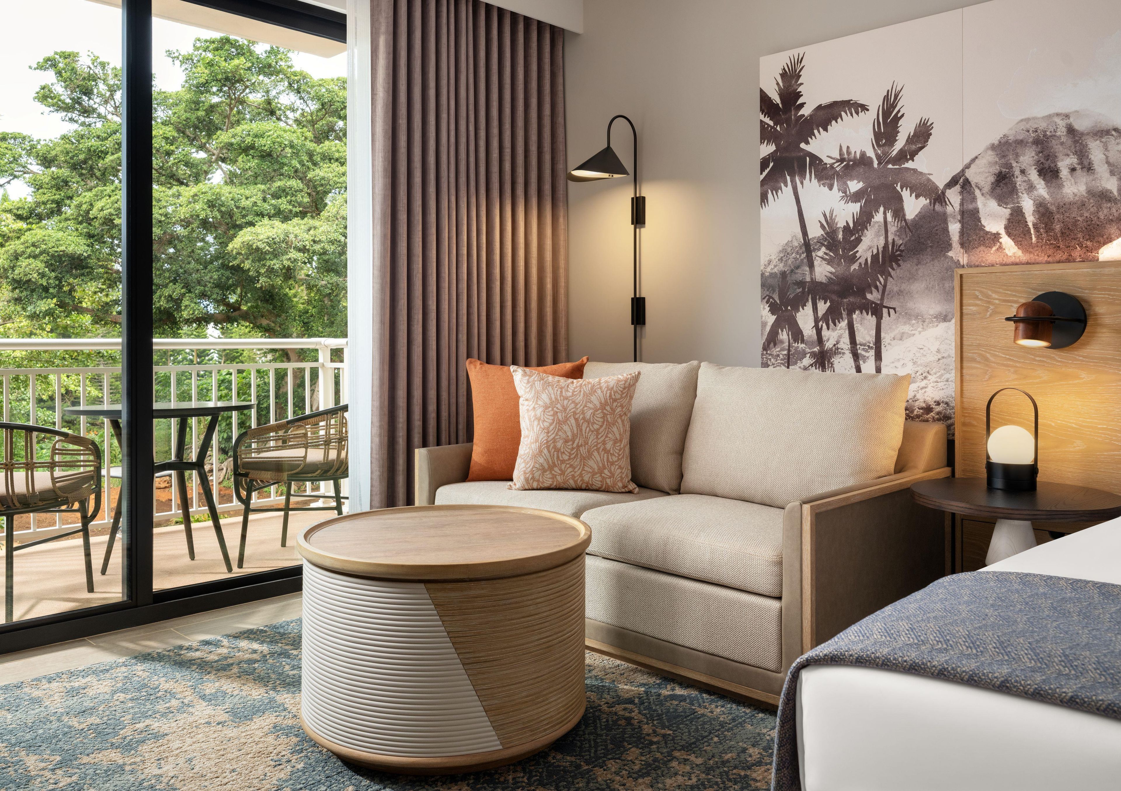 Habitación de hotel con sofá, una mesita redonda, lámpara y vistas al exterior.
