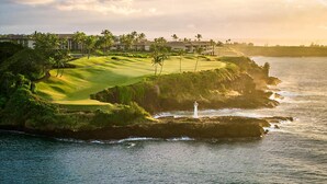 A coastal golf course with a lighthouse, ocean views, and a building complex in the background. - Hale Hokuala Kauai, Curio Collection By Hilton (Lihue)