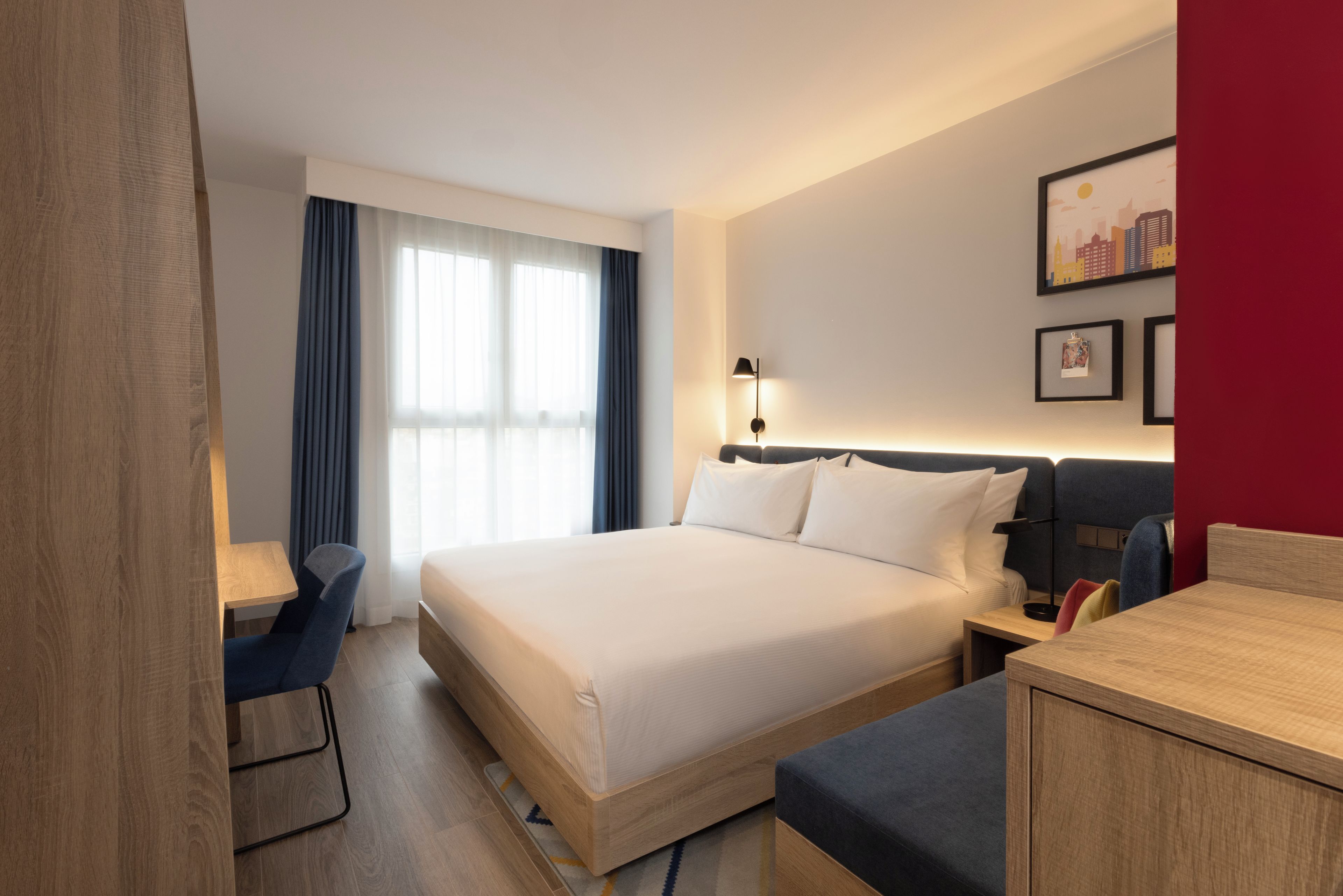 Ein Hotelzimmer mit Bett, Schreibtisch, Stuhl, Nachttisch und Lampe.