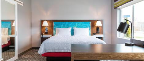 A hotel room with a bed, bedside tables, a desk, a chair, and a window with curtains.