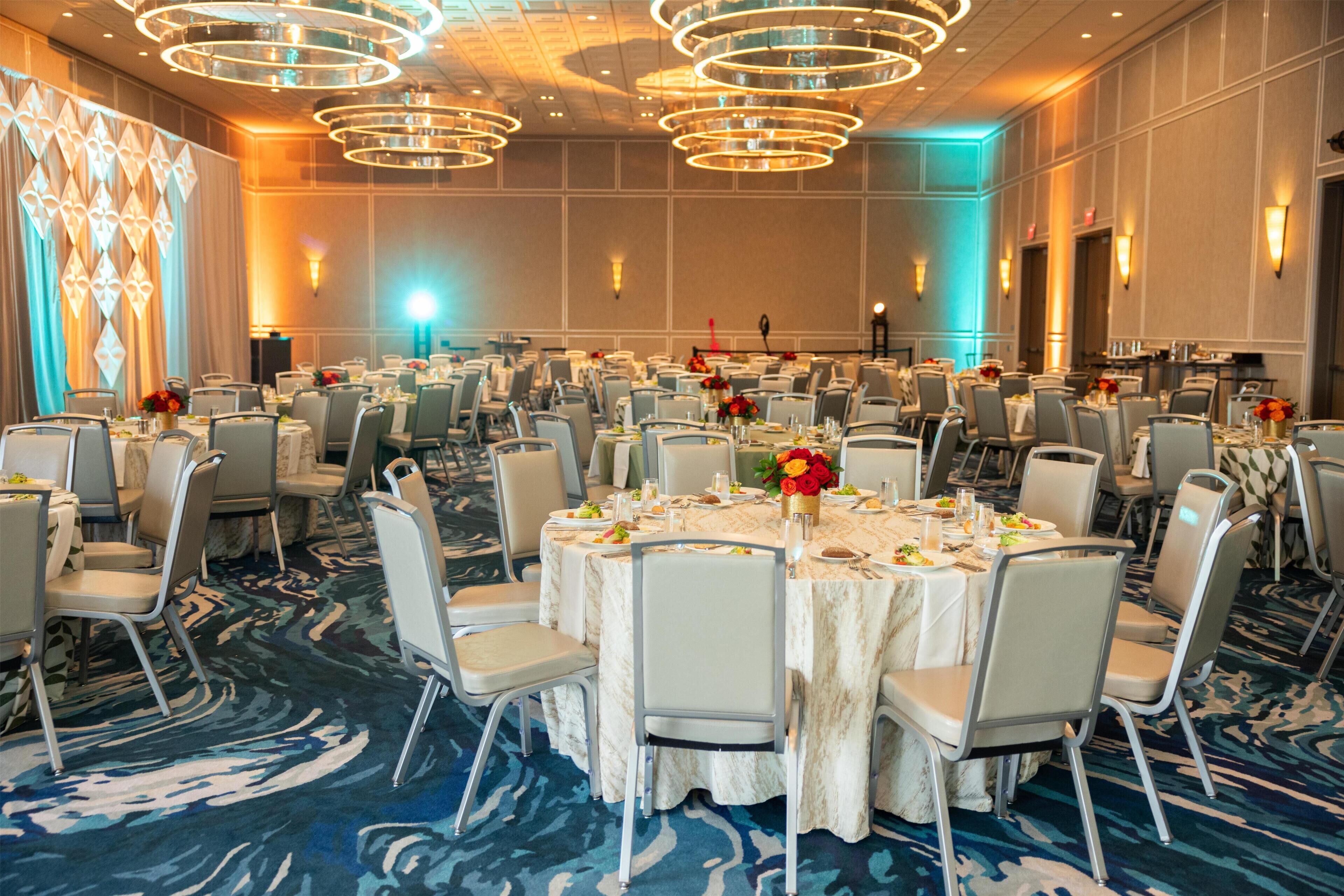 Un salón de banquetes con mesas redondas, sillas y una alfombra estampada.
